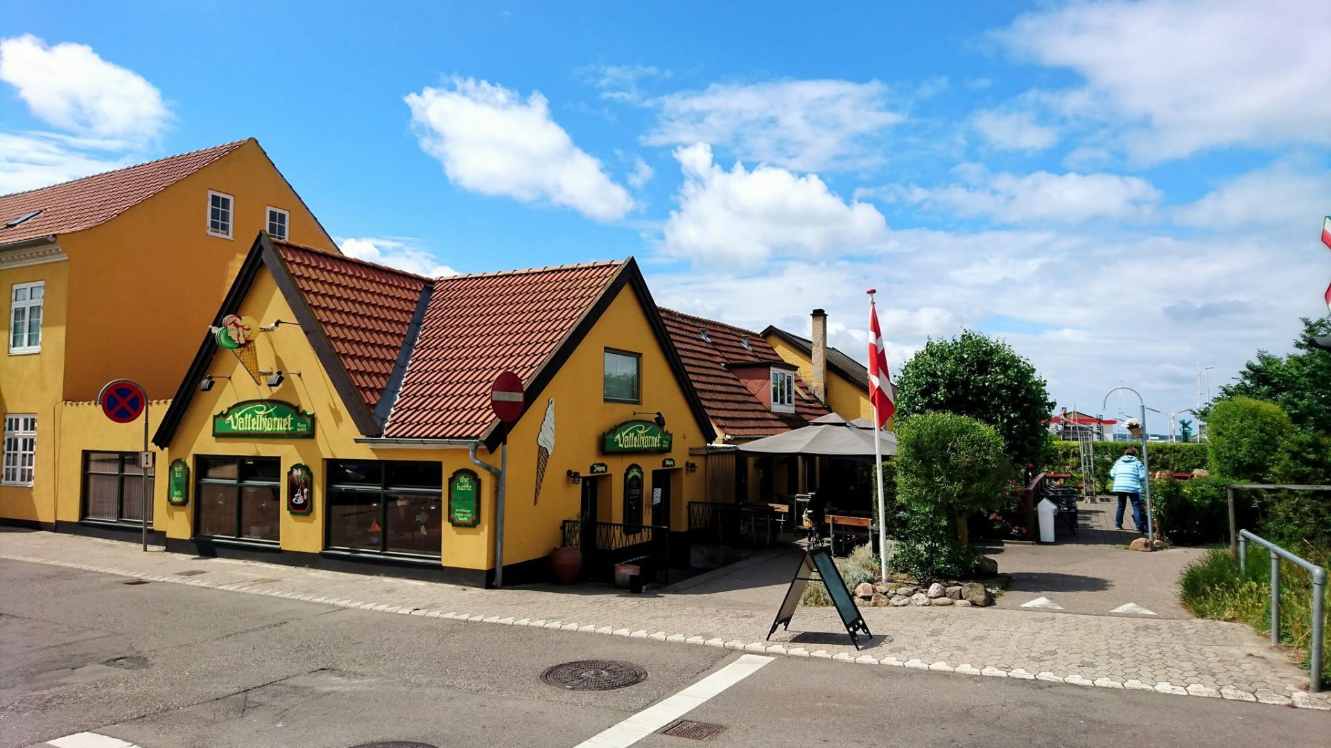 Vaffelhjørnet set fra vejen — gult hus med rødt tegltag og dansk flag